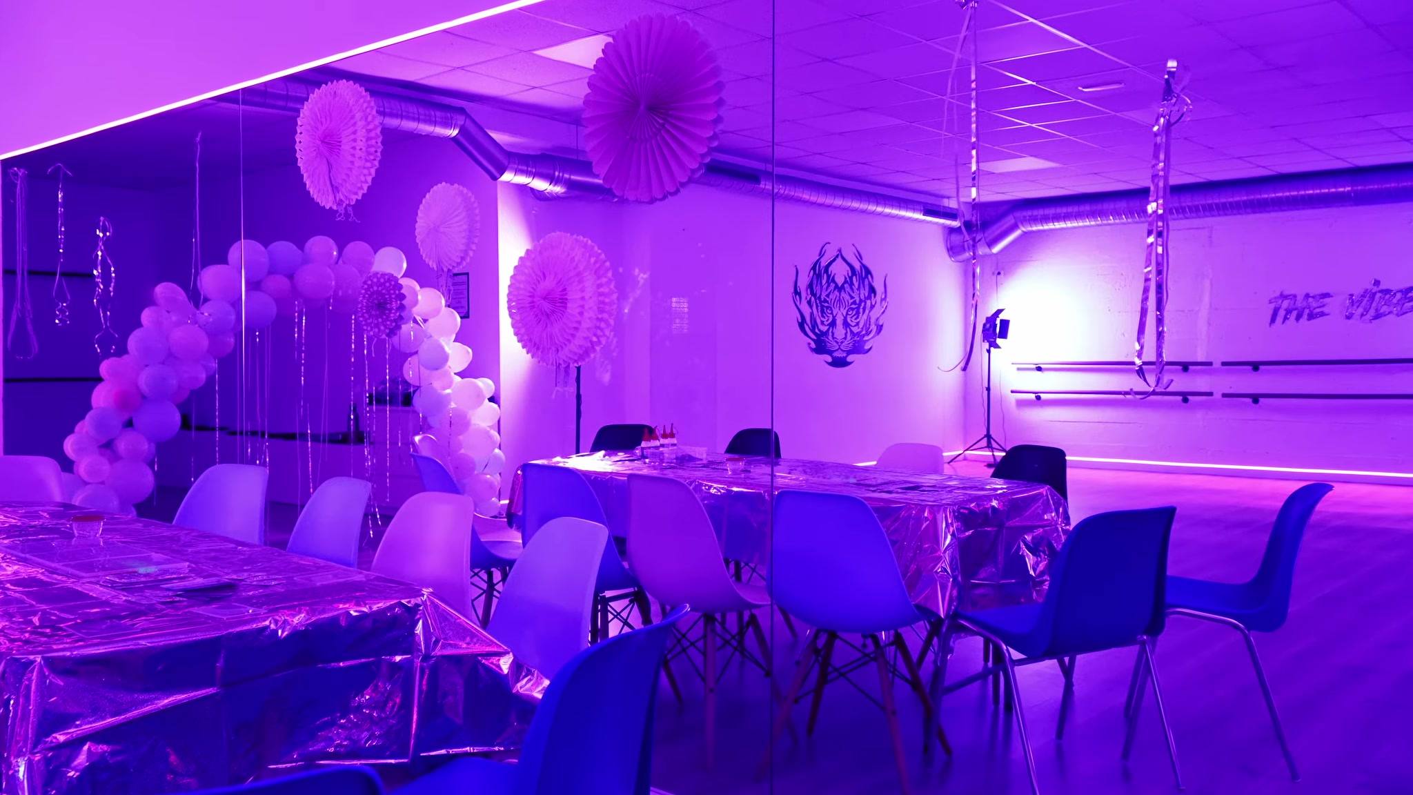 Sala de The Vibe decorada para un cumpleaños, con arco de globos, mesa y luz morada