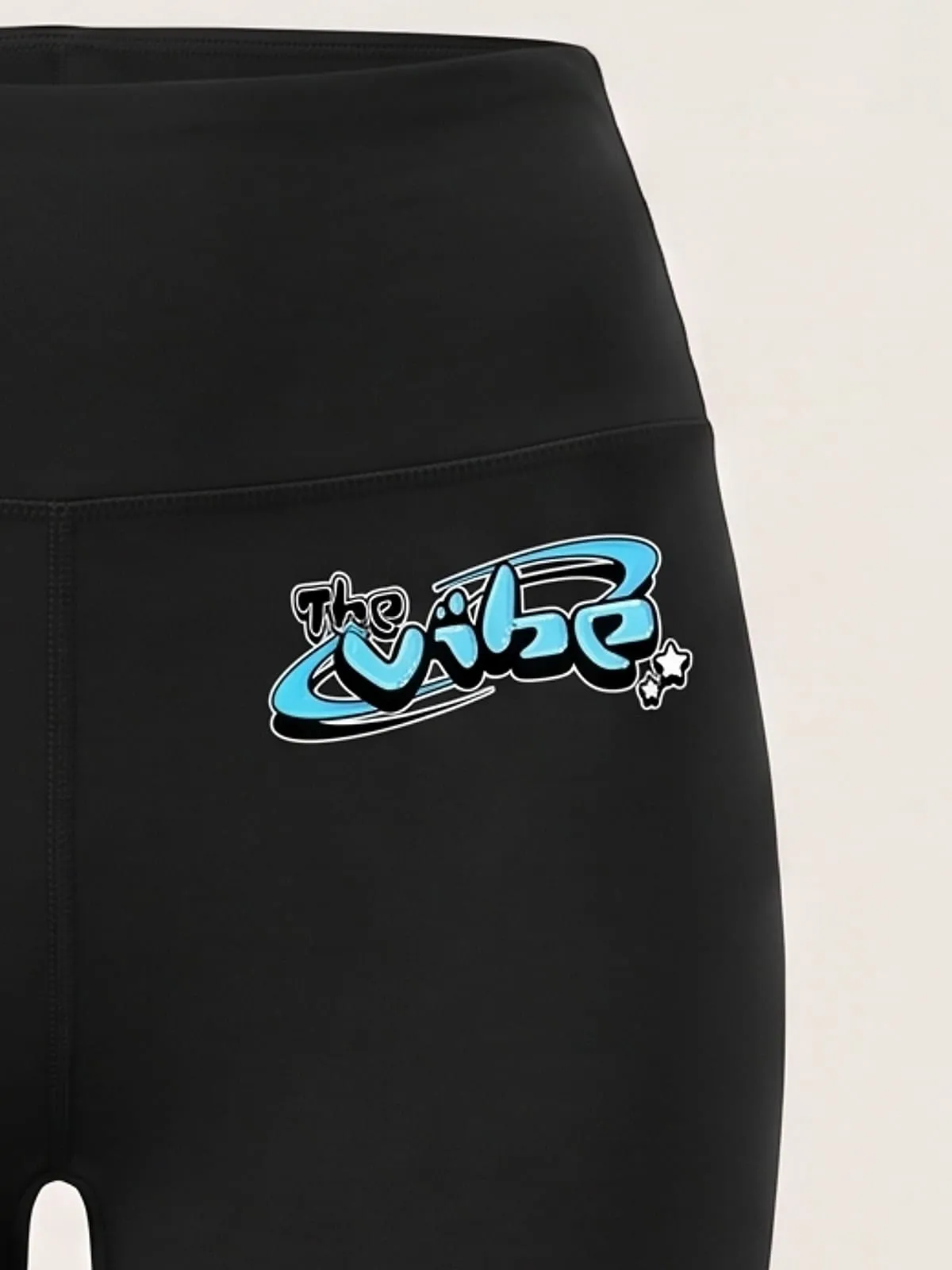 Detalle del logo de The Vibe en cian estampado en los leggings negros