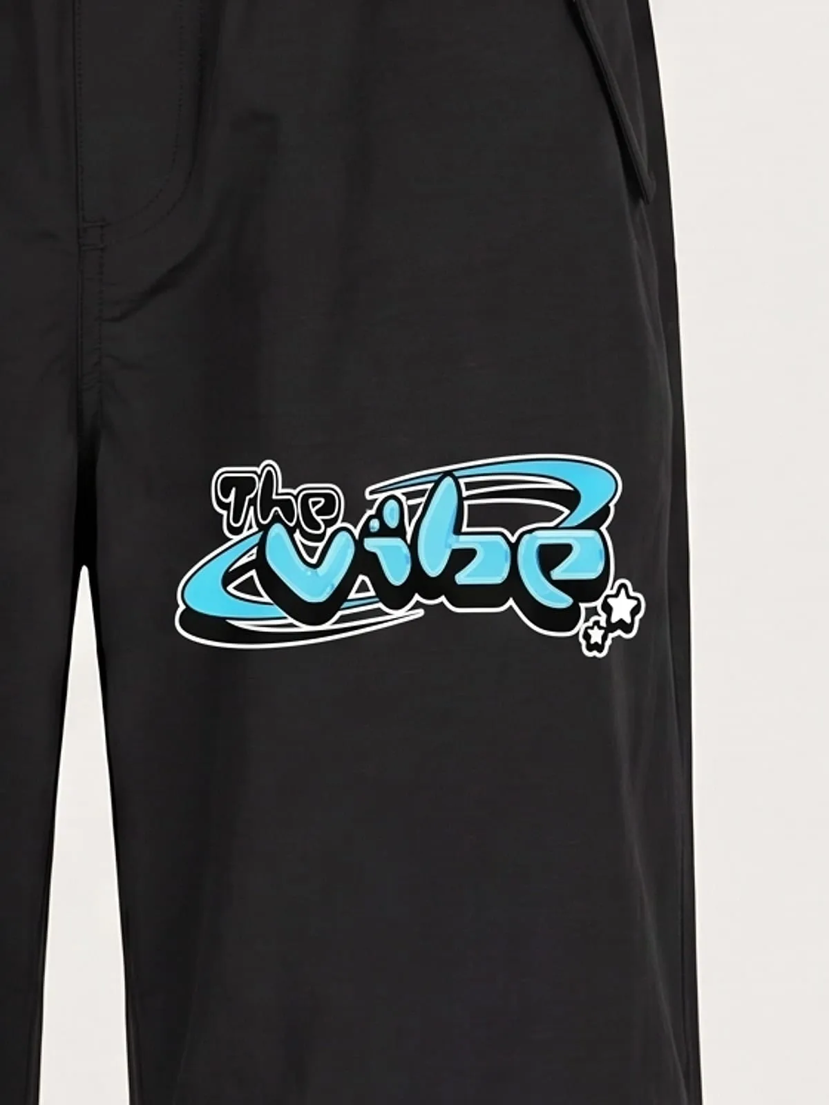 Detalle del logo de The Vibe en cian estampado en el pantalón ancho negro