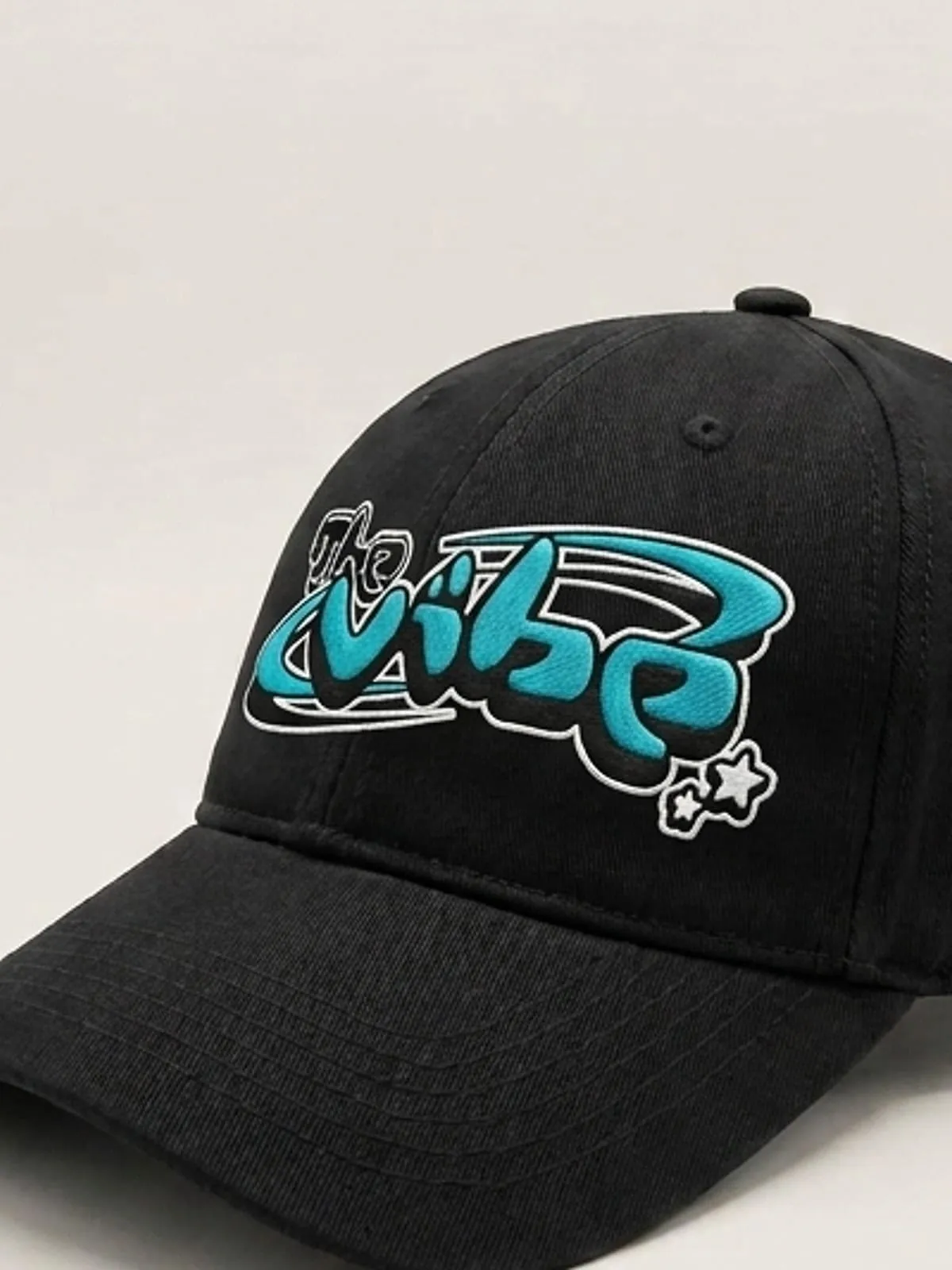 Detalle del logo de The Vibe en cian bordado en la gorra negra