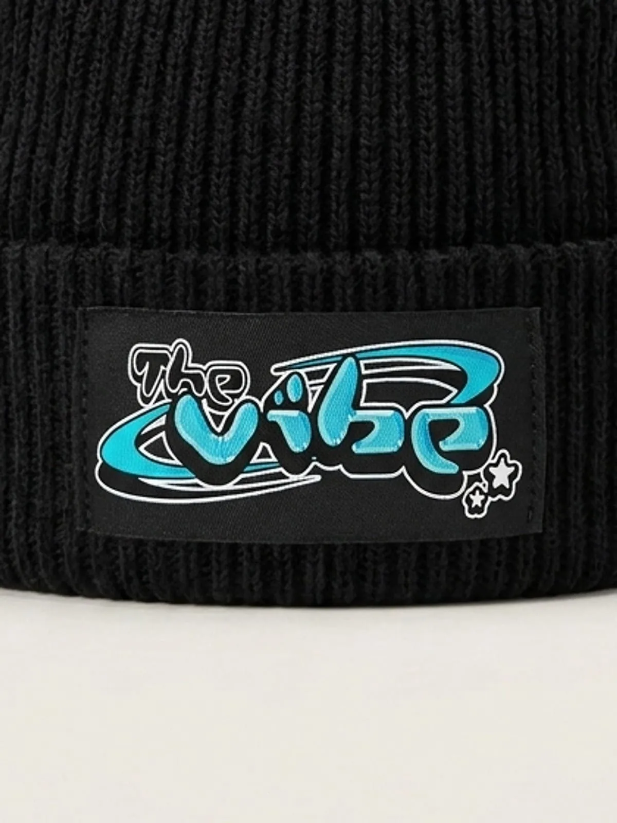 Detalle de la etiqueta tejida con el logo de The Vibe en cian en el gorro negro