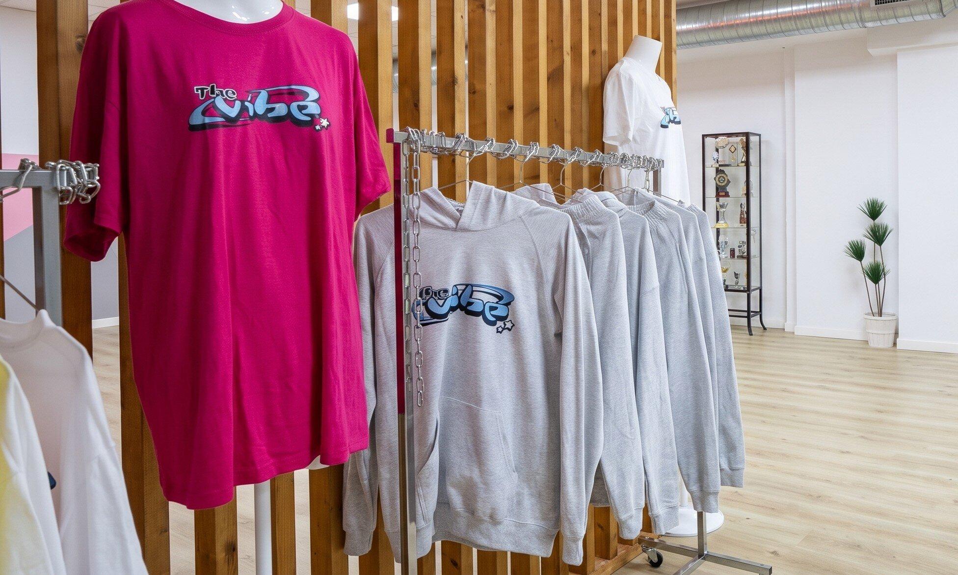 Sudaderas y camisetas con el logo de The Vibe colgadas en la tienda del studio