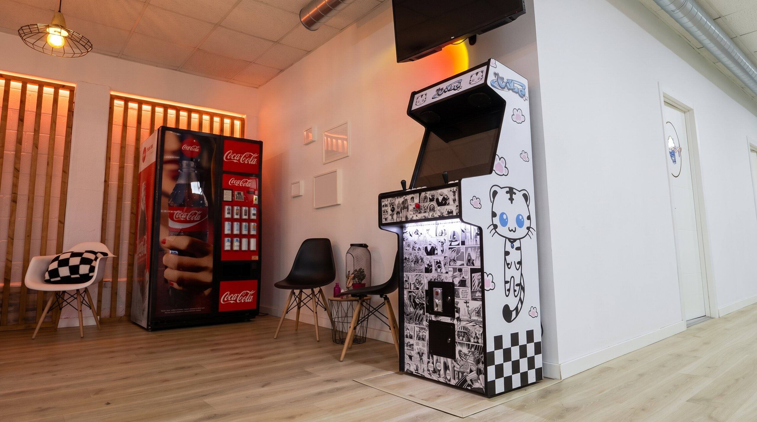 Zona común del estudio con máquina recreativa, nevera de bebidas y sillas